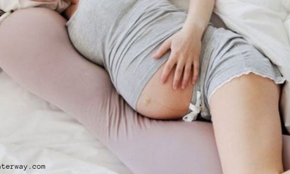 A women with pregnancy with her hand on wombs lying in a maternity pillow