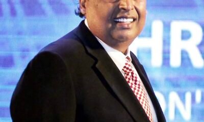 Mukesh Ambani in a dark suit with a patterned tie standing in front of a blue background